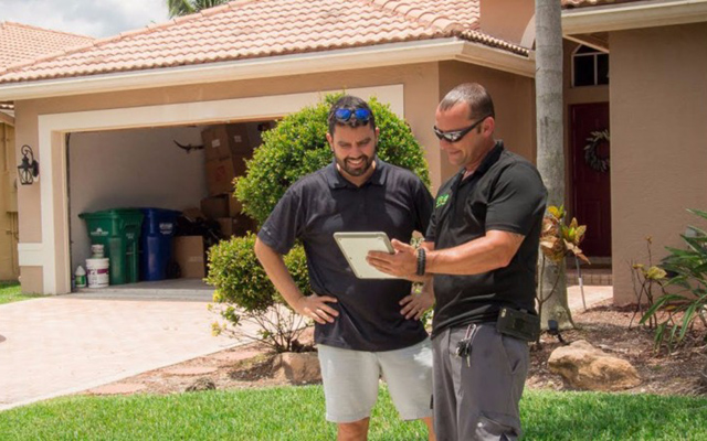 two men looking at documentation outside of a house